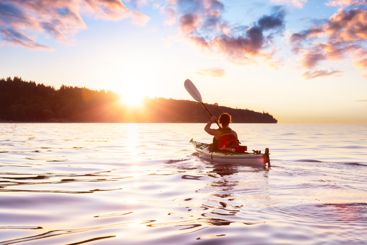 Woman on a sea kayak is paddling in the ocean during a colorful and vibrant sunset. Taken in Jericho, Vancouver, British Columbia, Canada. Concept: Adventure, Holiday, Vacation, Lifestyle, Freedom